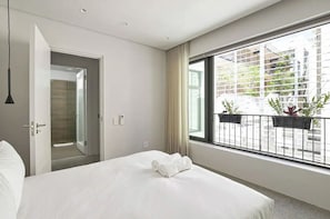 A hotel room with a large bed, a door leading to a bathroom, and a balcony with plants. - 2 Bedroom Elegant Bo-Kaap Escape (Cape Town)
