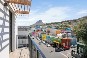 A balcony with a view of a colorful town, a mountain in the background, and parked cars on the street. - 2 Bedroom Elegant Bo-Kaap Escape (Cape Town)