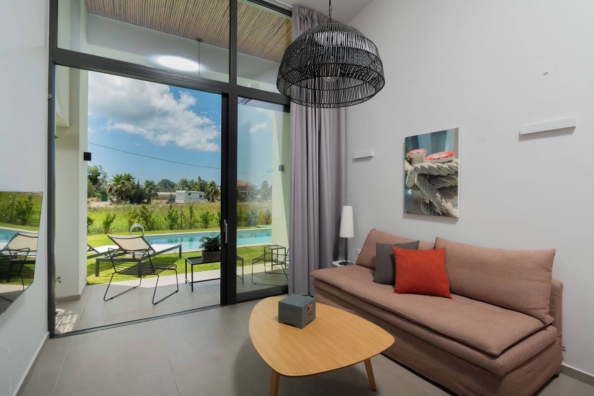 A modern living room with a sofa, a table, and a view of a swimming pool.
