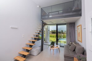 A modern interior with a staircase, a sofa, a coffee table, and a view of a pool. - Sevene Villas (Kourouta)