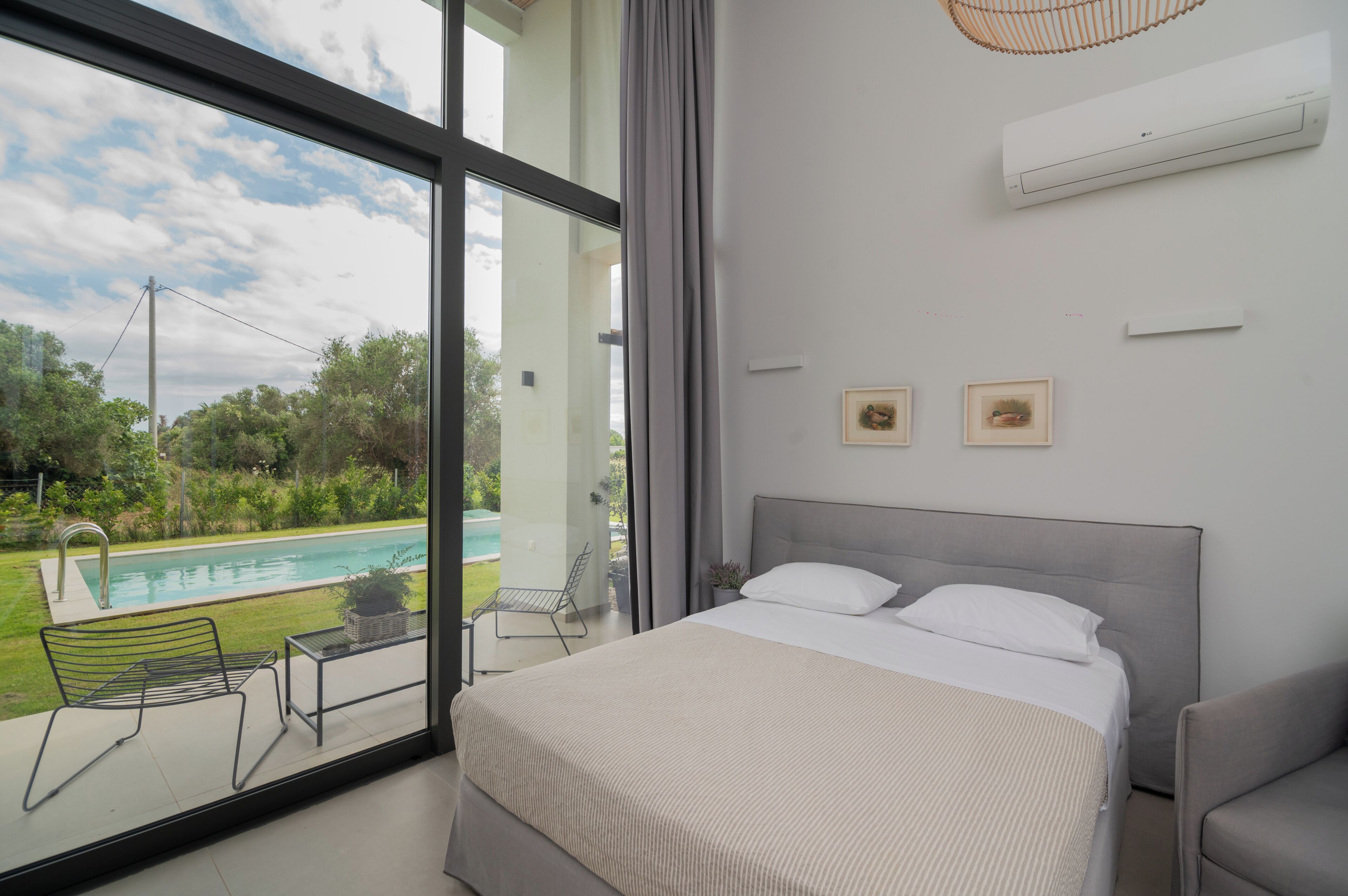 Ein Schlafzimmer mit großem Fenster, einem Bett, einem Sessel und einem kleinen Tisch.