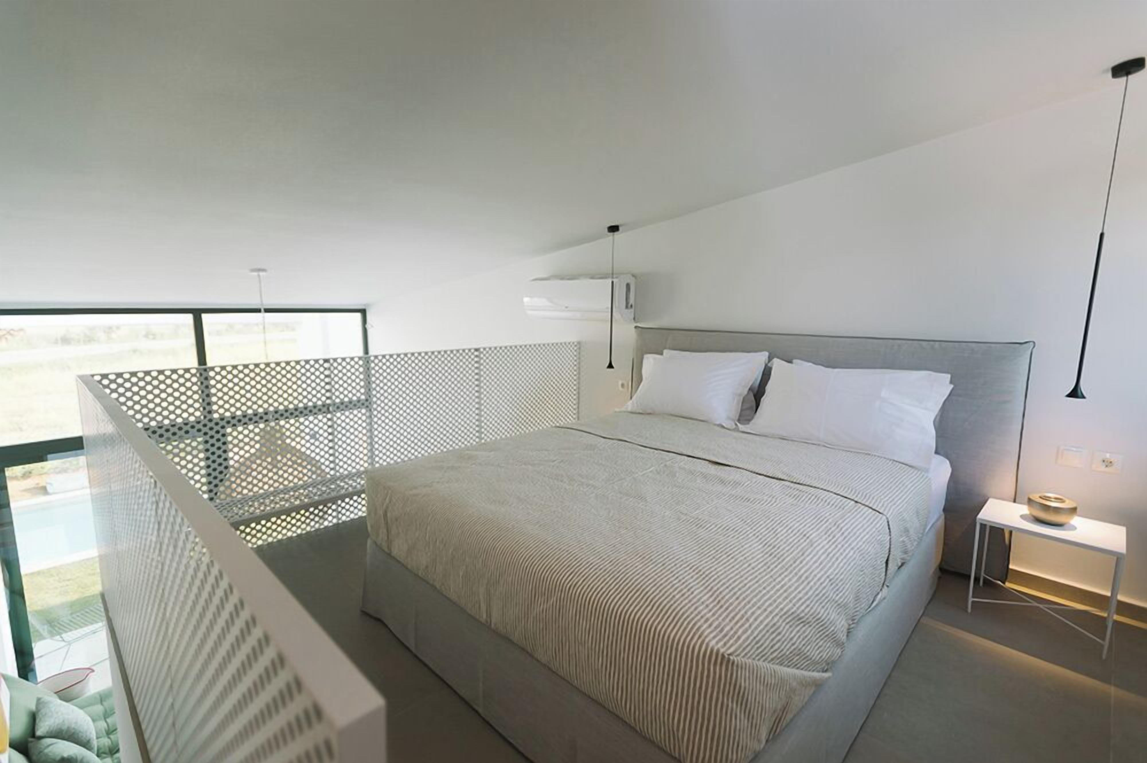 A modern bedroom with a large bed, a bedside table, a hanging light, and a balcony with a mesh railing.