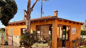 A single-story house with a tiled roof, a front door, and a small garden with flowers and a fountain. - Independent House for Two with Pool and Garden (El Turó)