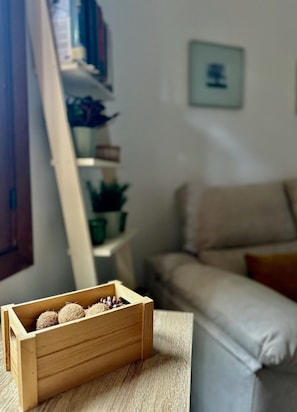 Ein Holzkasten mit kugelförmigen Gegenständen auf einem Tisch, ein Sofa, ein Bücherregal und ein gerahmtes Bild an der Wand.