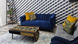 A living room with a blue sofa, a patterned coffee table, and a geometric patterned wall. - Comfortable 3BR Family Home | Free Parking Included (Chester)