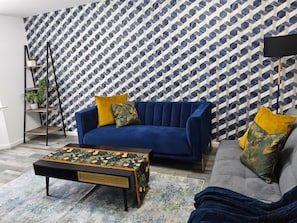 A living room with a blue sofa, a patterned coffee table, and a geometric patterned wall. - Comfortable 3BR Family Home | Free Parking Included (Chester)