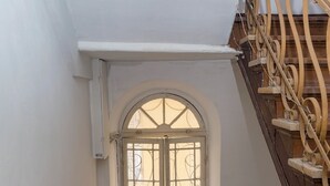 Eine Treppe mit schmiedeeisernem Geländer, ein kleines Fenster mit Metallgitter und einem Schachbrettmuster auf dem Boden.