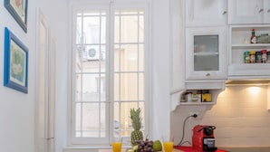 Eine Küche mit Fenster, Obstschale, Kaffeemaschine und weißen Schränken.