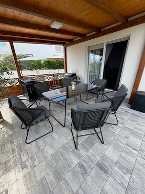 A covered patio with a table and chairs, a grill, and a view of the street. - Villa Len Mar Zadarvillas (Vir)