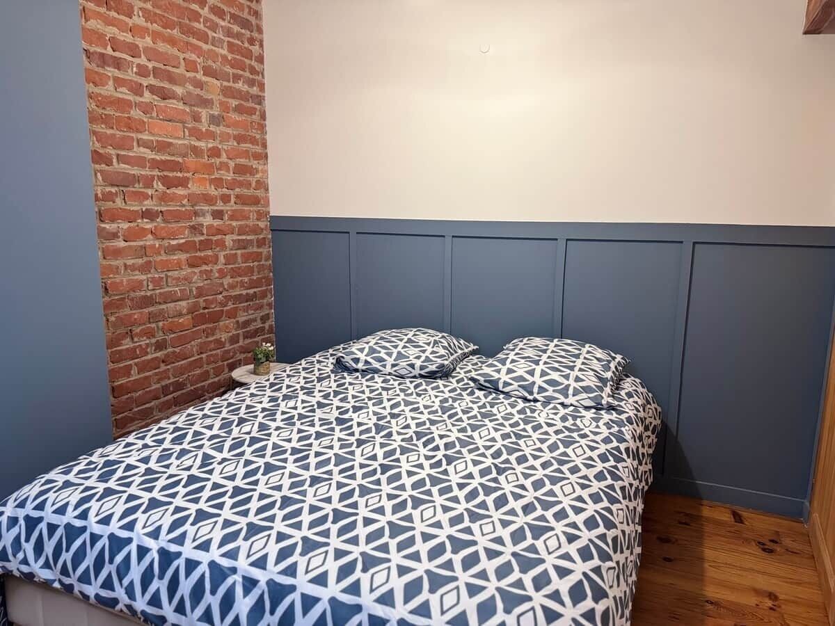 A bed with a geometric patterned bedspread, a brick wall, and a blue headboard.