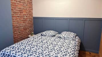 A bed with a geometric patterned bedspread, a brick wall, and a blue headboard.