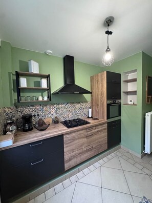 A kitchen with a wooden countertop, black cabinets, a black range hood, and a hanging light fixture.
