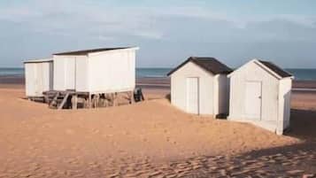 Eine Reihe von Strandhütten mit einem Sandstrand und dem Meer im Hintergrund.