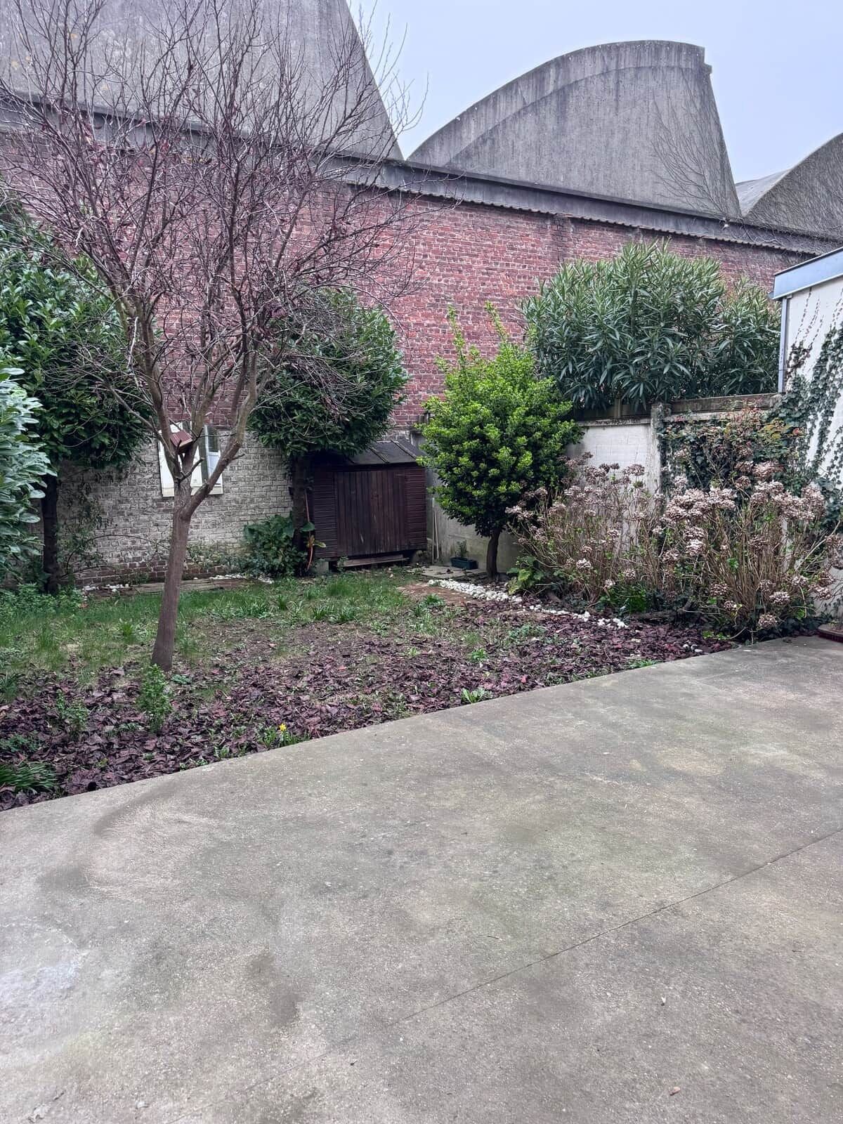 A concrete driveway leading to a brick building with a metal roof.