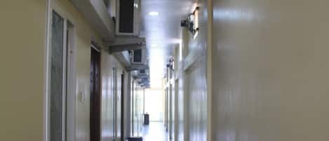 A long, narrow hallway with doors on both sides, a ceiling with recessed lighting, and a shiny floor.