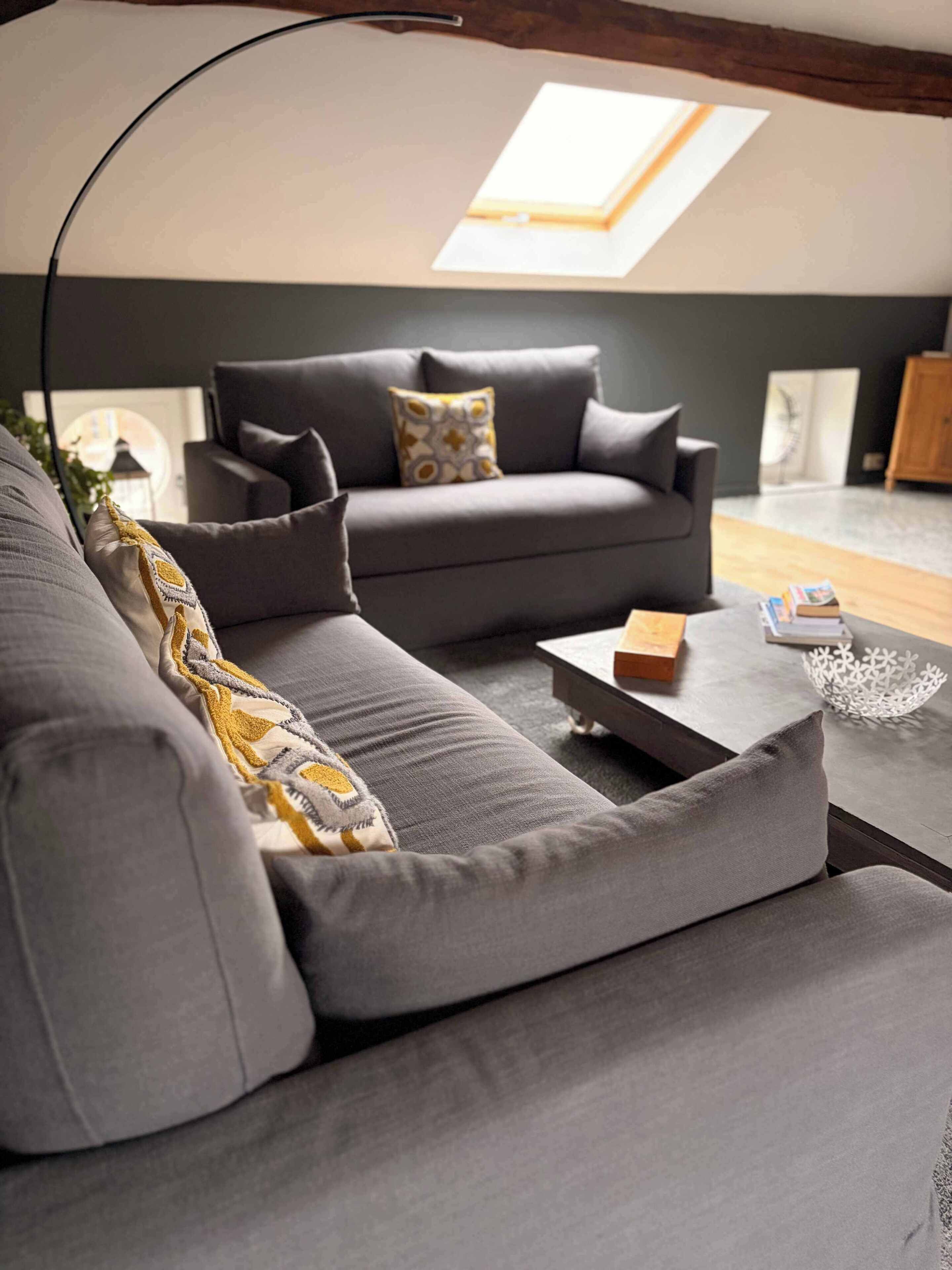 A modern living room with a grey sofa, a coffee table, and a skylight.