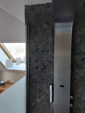 A modern bathroom with a stone mosaic wall, a stainless steel shower, and a skylight.