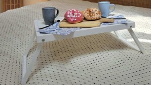 Een bed met een dienblad donuts, twee mokken en een kaars op een nachtkastje.
