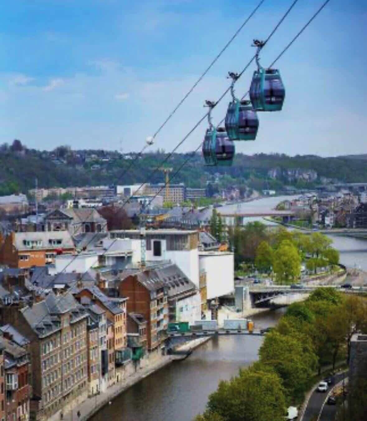 A cable car system over a river with buildings and a bridge in the background.
