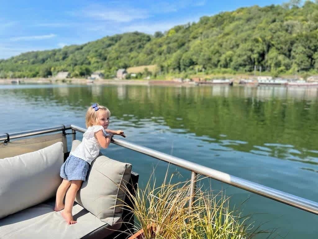 A child on a boat with a view of a lake and forested hills.