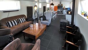 Een modern interieur met een bank, fauteuil en een eettafel. Achterin is een keukenruimte te zien.