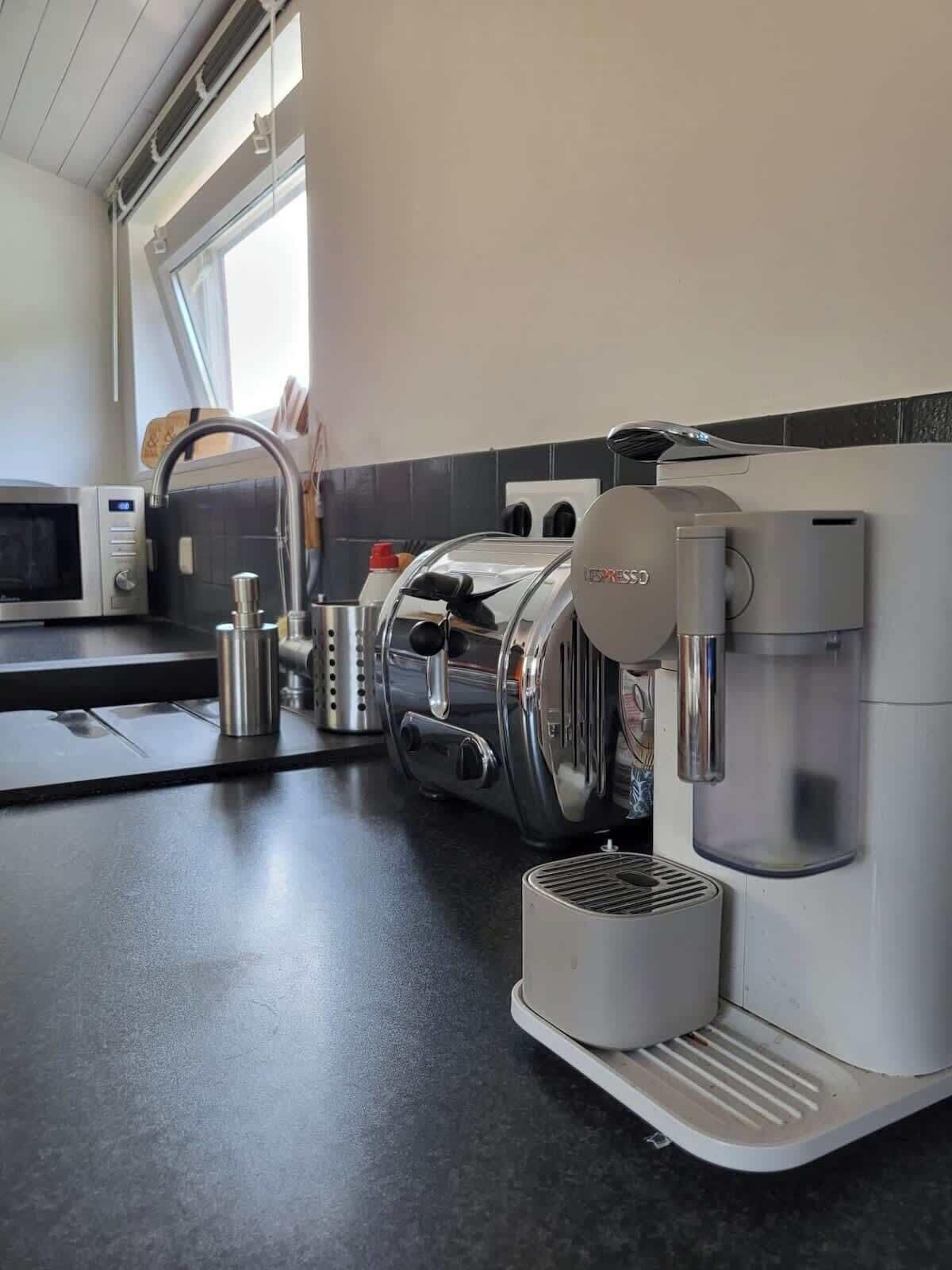 Een keuken met een koffieapparaat, een magnetron en een raam.