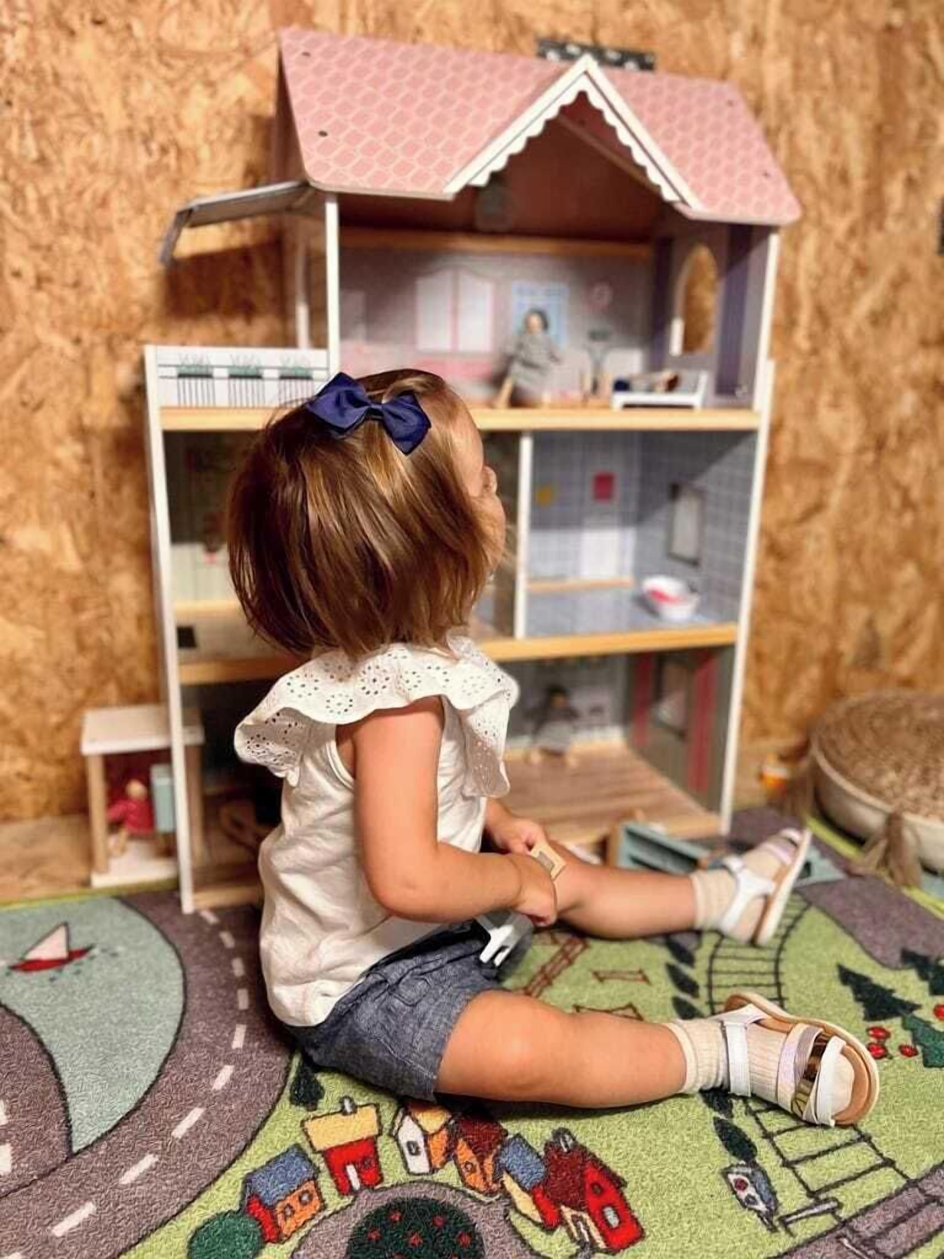 A child sitting on a colorful rug in front of a dollhouse with shelves.