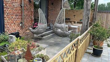 A brick building with a wooden deck, two hanging chairs, and various potted plants.