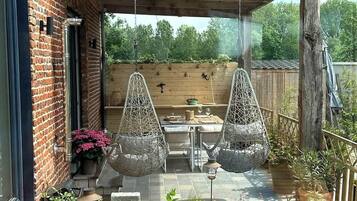 Un porche cubierto con sillas colgantes, una mesa pequeña y un jardín con un estanque.