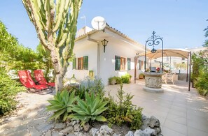 A white building with green shutters, a satellite dish, and a stone patio with red chairs and plants. - Casa Cactus, Can Picafort, Mallorca (Can Picafort)