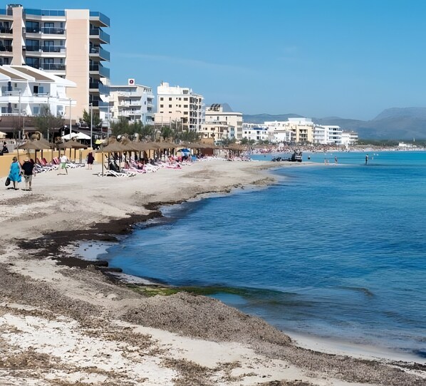 A beach with buildings in the background, clear skies, and a calm sea. - Casa Cactus, Can Picafort, Mallorca (Can Picafort)
