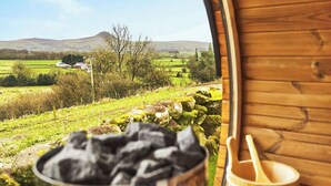 A rustic wooden interior with a view of a green landscape, a metal container with charcoal, and a wooden spoon.