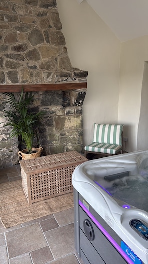 A stone fireplace, a wicker basket, a striped chair, and a hot tub.