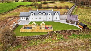 A large white house with a stone chimney, a wooden play area, and a stone wall surrounding the property.