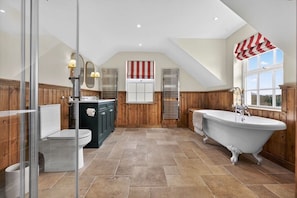 A bathroom with a freestanding bathtub, a toilet, a vanity with a mirror, and a window with a view.