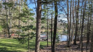 A forested area with a lake, a dock, and a boat. - Cozy lakefront cabin, TONS of amenities; dog friendly; 15 mins to downtown TC (Traverse City)