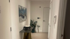 A hallway with a white door, a painting on the wall, a small table with a bowl, and a potted plant. - Business Suite Lux 2 Bed Apartment in St Albans (St Albans)