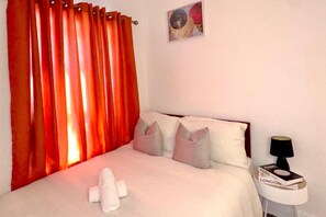 Ein Hotelzimmer mit einem Bett, Kissen, einer Nachttischlampe, einem Nachttisch und einem roten Vorhang.