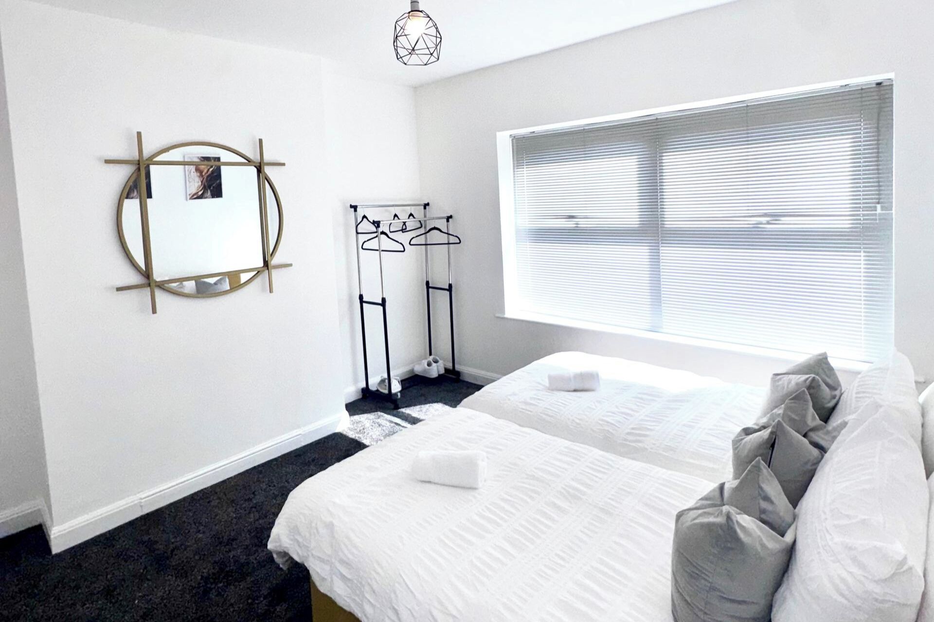 A hotel room with two beds, a window with blinds, a mirror, and a coat rack.
