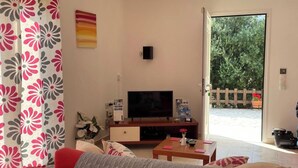 Un salon comprenant un canapé, un téléviseur, une table basse et une porte donnant sur un jardin.
