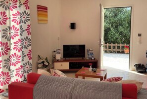 Ein Wohnzimmer mit einer Couch, einem Fernseher, einem Couchtisch und einer Tür, die in einen Garten führt.