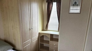 A bedroom with a bed, a wardrobe, a window with curtains, and a small desk with drawers. - Caravan Situated on Coastfields, Ingoldmells (Skegness)