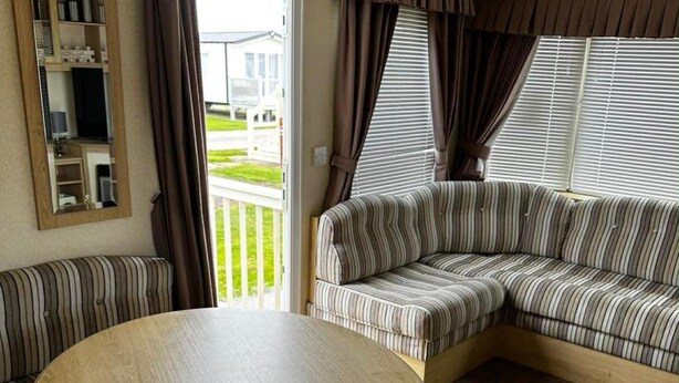 A room with a striped sofa, a round wooden table, a mirror, and a window with blinds. - Caravan Situated on Coastfields, Ingoldmells (Skegness)