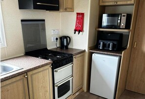 A compact kitchen with a stove, oven, microwave, and a small refrigerator.