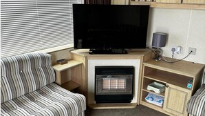 A living room with a television, fireplace, striped sofa, and wooden shelves. - Caravan Situated on Coastfields, Ingoldmells (Skegness)
