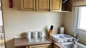A compact kitchen with wooden cabinets, a granite countertop, a sink, and a window. - Caravan Situated on Coastfields, Ingoldmells (Skegness)