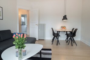 Ein modernes Wohnzimmer mit einer Couch, einem Esstisch mit Stühlen, einer Vase mit Blumen und einer Heizung.
