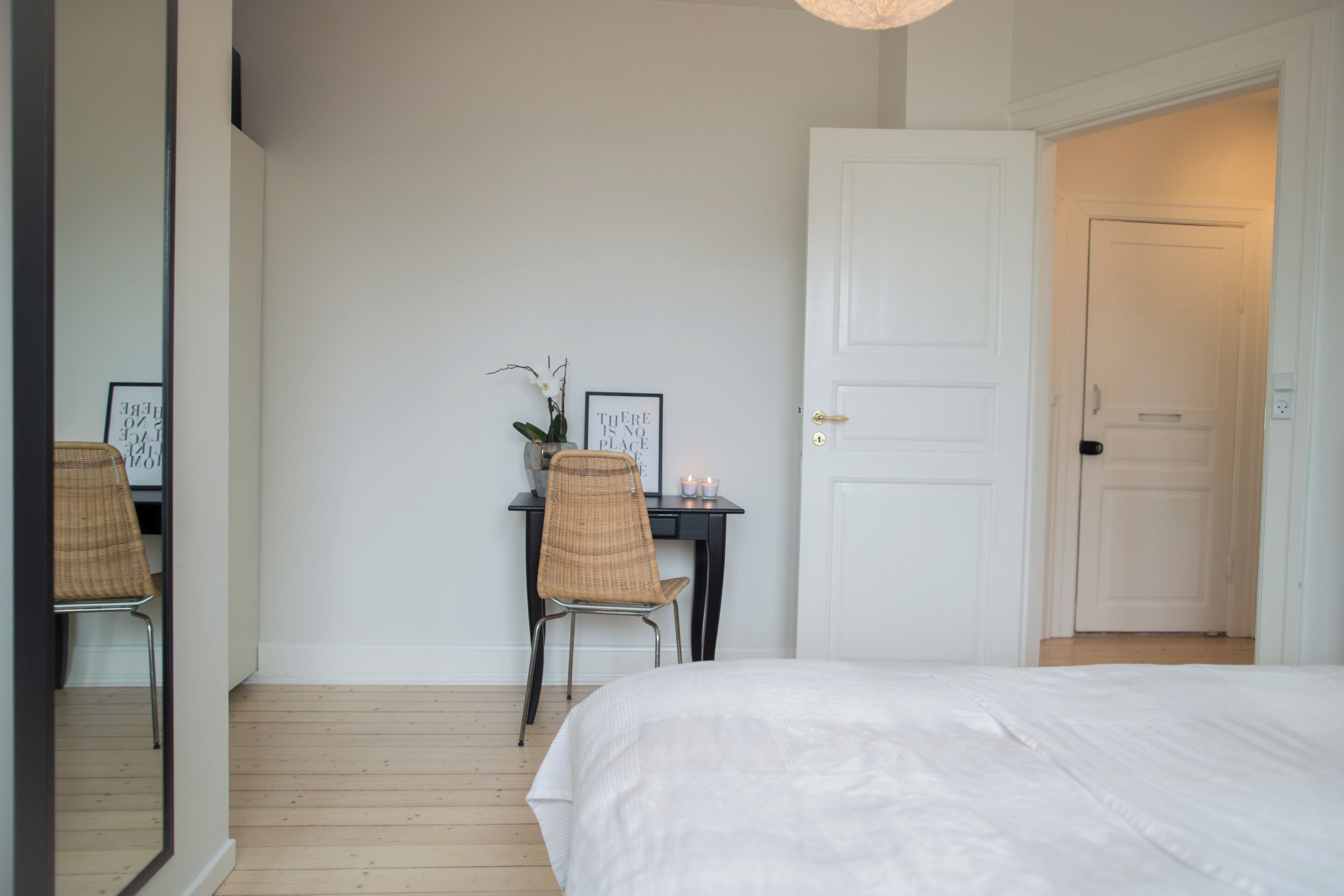 A bedroom with a bed, a desk with a chair, a mirror, and a door.