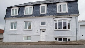 A two-story building with a white facade, numbered 12, featuring multiple windows and a central door. - Apartment Sleeps 2 With Garden (Norresundby)