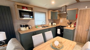 A compact kitchen with a microwave, toaster, sink, and stove. There is a dining table with chairs and a basket on it. - Vintage 121 - Southview Holiday Park Skegness (Skegness)